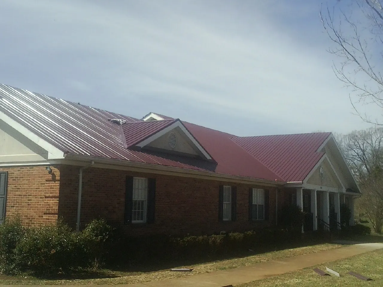 Red metal roof with gabled entries on a long brick building, from a Hail Damage Roof Repair job in Kinsale