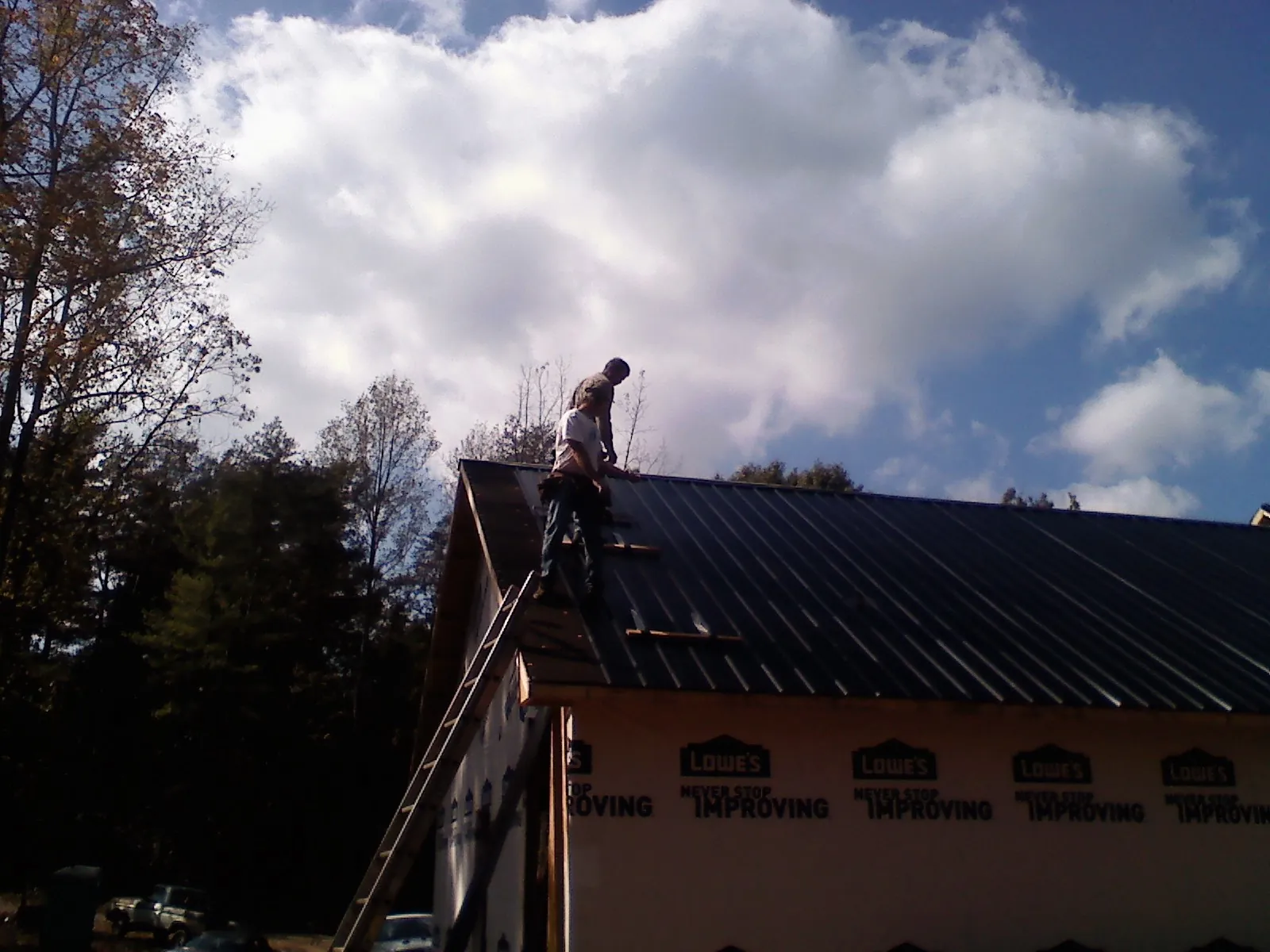 Roofer fastening dark metal panels high against a cloudy sky, from a Roof Inspection job in Kinsale