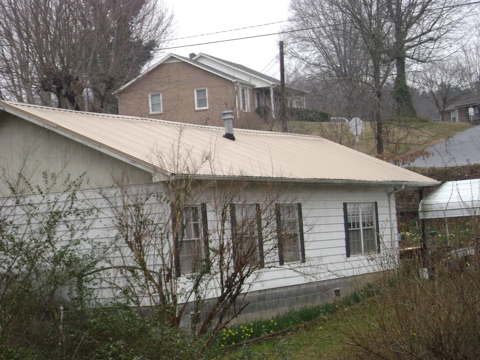 Tan metal roof on a white sided house set into a hillside — Commercial Roofing by Roofing Brothers in Kinsale