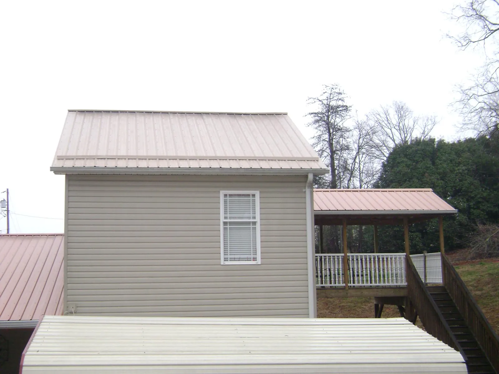 Tan metal roofs on a two story addition and attached porch, from a Roof Replacement job in Kinsale